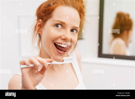 Young Pretty Red Haired Woman With White Toothbrush In Her Hand Licking