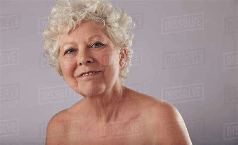 portrait of beautiful naked senior woman looking happy against grey