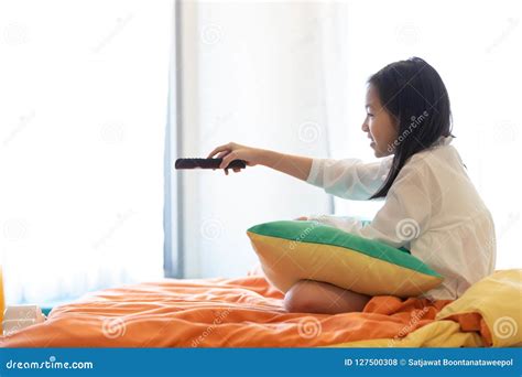 asian girl watching tv lying on bed with remote control in hand stock
