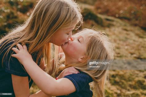 two cute blond sisters kissing outdoors high res stock