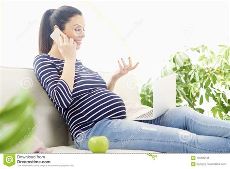 pregnant woman talking on her mobile phone and using notebook stock
