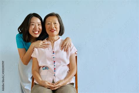 Senior Asian Mother Sitting On The Chair With Asian Young Daughter With