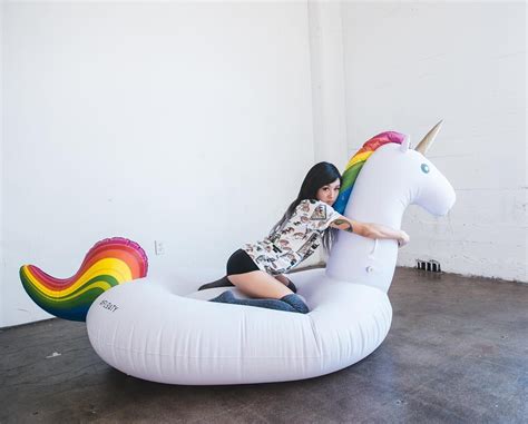 A Woman Is Sitting On An Inflatable Unicorn Shaped Chair With A Rainbow