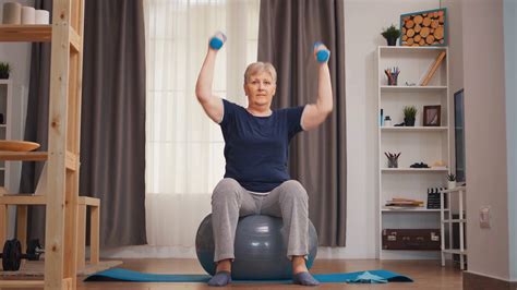 senior woman lifting dumbbells sitting on fitness ball in