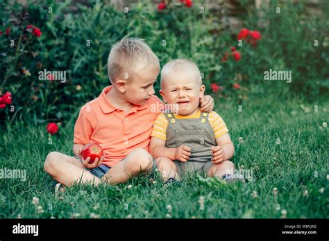 two brothers sitting together on grass in park outside sharing apple