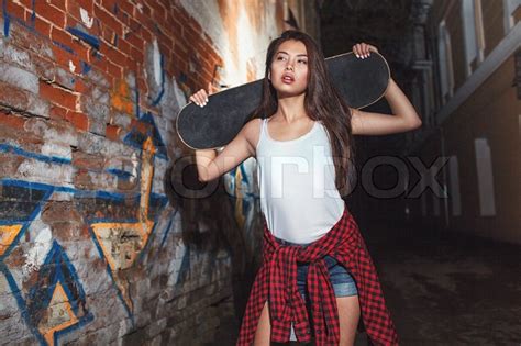 beautiful asian teen girl with skate board on shouldres outdoors urban lifestyle stock