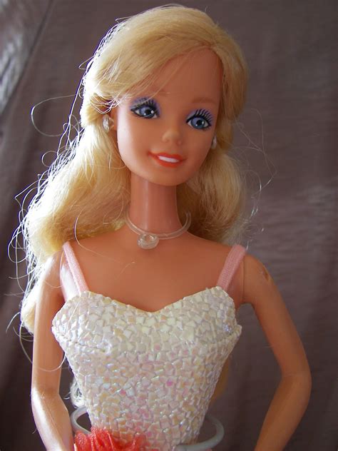a blonde barbie doll wearing a white dress and red flower in her hand