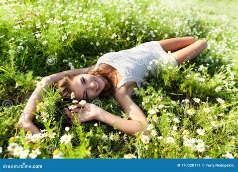 Young Brunette Woman Lying On Grass And Flowers And Smiling On Summer