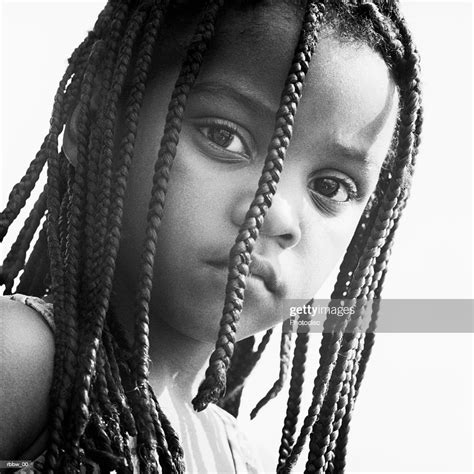 A Young African American Girl Peers Through Her Braids With A Look Of