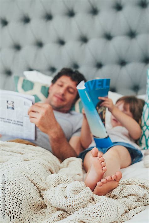 dad and daughter bonding while reading in bed together by aila images
