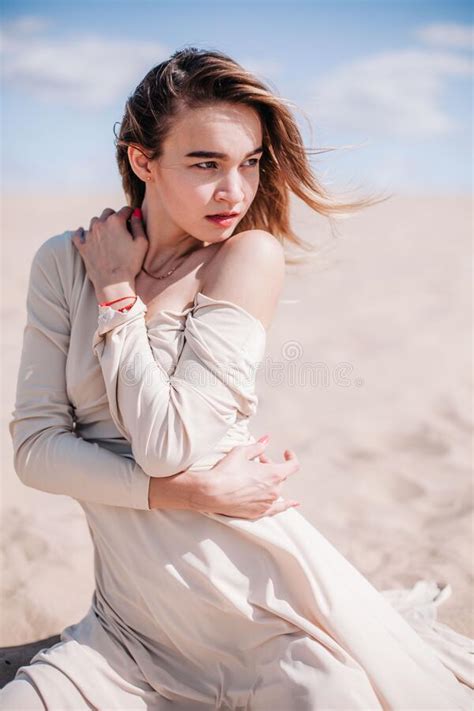 A Young Slender Girl In A Beige Dress Poses In The Wind In The Desert