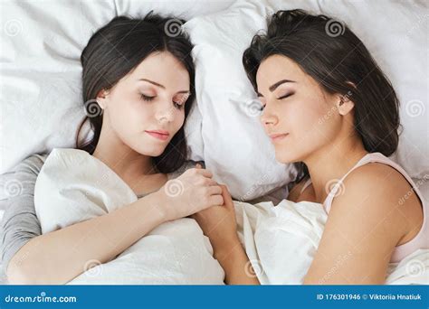 lesbian couple in bedroom at home lying under blanket holding hands
