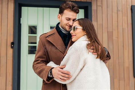 loving wife wearing beige coat and glasses hugging her beloved stock