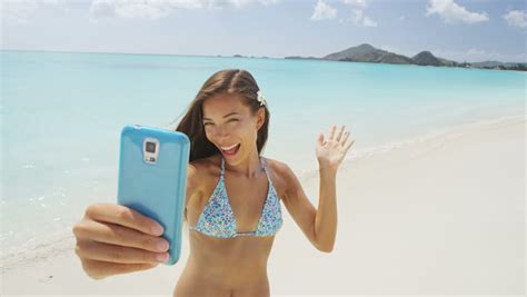 woman taking smart phone selfie video or photo bikini travel girl on beach smiling happy on