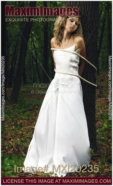 Photo Of Young Bride In Wedding Dress Tied To A Tree With Ropes In A