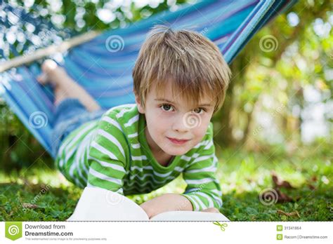 jongen die  hangmat liggen en een boek lezen stock foto image  kijkt camera