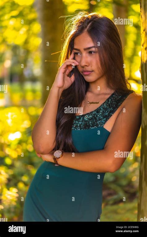 Young Brunette Latina With Long Straight Hair Leaning Against A Tree In