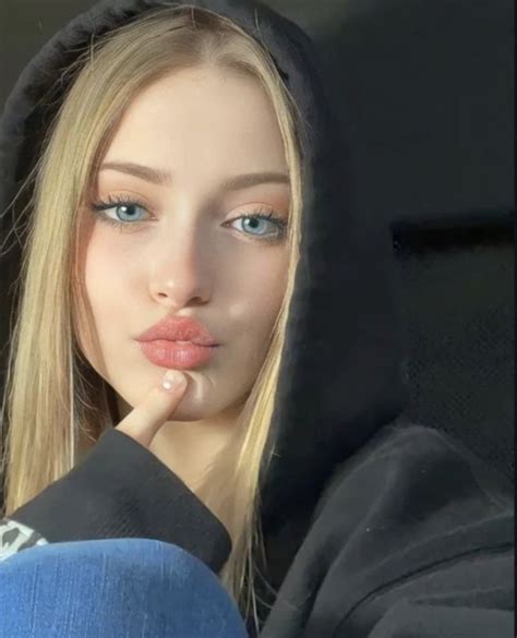 A Woman With Long Blonde Hair And Blue Eyes Wearing A Black Hoodie