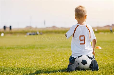 kindzitting op voetbalbal op de voetbalhoogte jong geitje  het letten op van sportenjersey