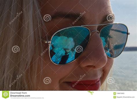a blonde woman smiles in a pair of blue sunglasses stock