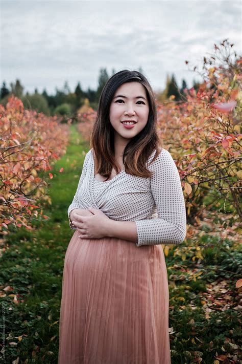portrait of pregnant asian woman outdoor in a park by stocksy