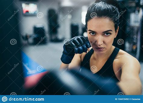 Front View Of Strong Brunette Attractive Female Trainer Punching A Bag