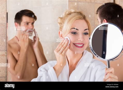 Portrait Of A Man Shaving And Her Wife Cleaning Her Face In Mirror At