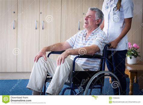 Female Doctor Carrying Senior Man On Wheelchair Stock