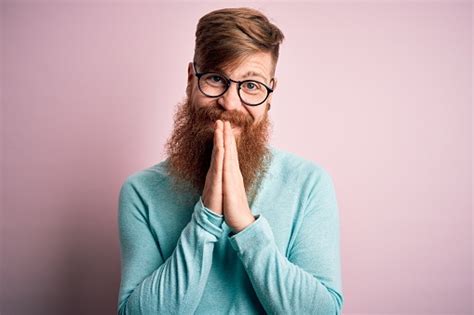 handsome irish redhead man with beard wearing glasses over pink