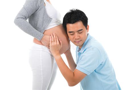 husband listening the belly of his pregnant asian wife isolated on white background stock image