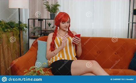 cheerful redhead girl sitting on sofa using smartphone share messages