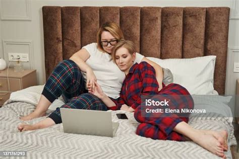Lesbian Couple In Pajamas Lies On The Bed In Front Of Them Open Laptop