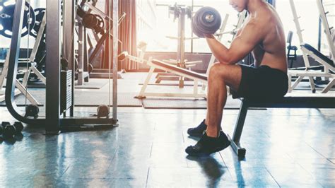 homem musculoso construído atleta malhando na academia sentado na máquina de levantamento de