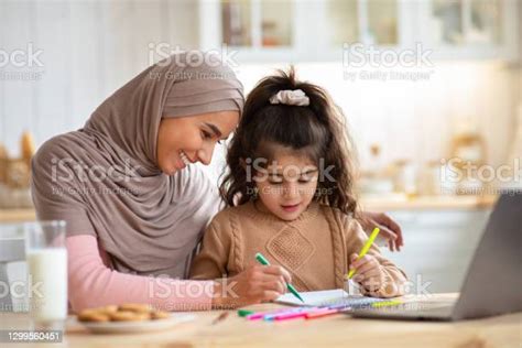 loving muslim mom in hijab drawing with her little daughter in kitchen