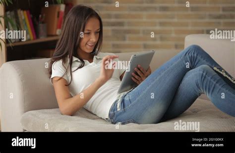 Cute Girl Relaxing On Sofa Using Touchpad Looking At Camera And Smiling