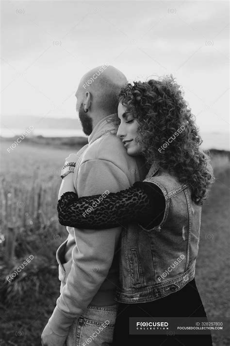 Man Embracing By Happy Curly Haired Girlfriend In Dress And Denim Vest
