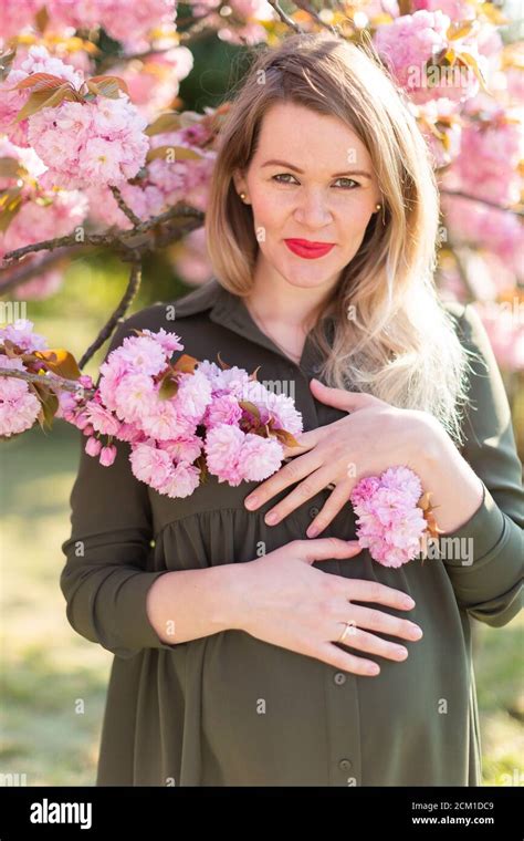 freckled blonde pregnant woman in the park at spring with sakura trees