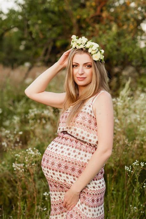 portrait of a pregnant blonde in nature in a wreath of white roses
