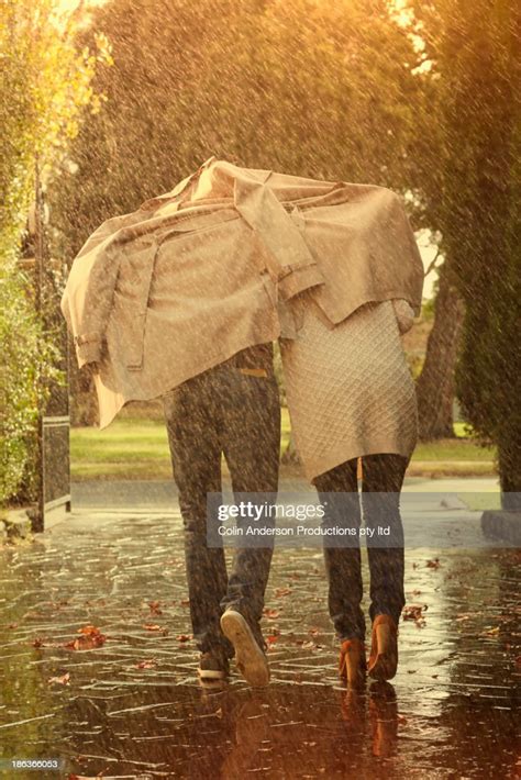 caucasian couple running under coat in rain photo getty images