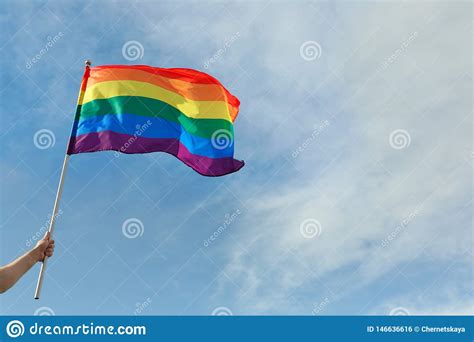 gay man holding rainbow lgbt flag against blue sky stock