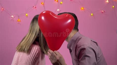 Couple In Love Man And Woman Kiss Each Other Hiding Behind A Balloon