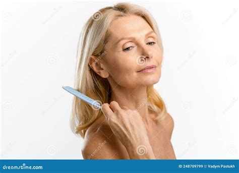 Elegant Serene Middle Aged Blonde Woman Combing With Crest Looks Down