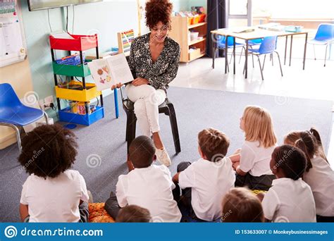 female teacher reading story to group of elementary pupils wearing