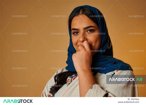 بورتريه لإمرأة عربية خليجية سعودية تضع يدها على فمها، تعابير وجه سعيدة