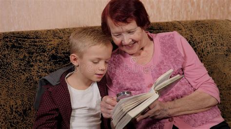 An Elderly Grandmother Reading A Book With Her Grandson Using A