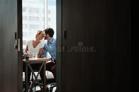 Two Co Workers Sitting At Office Desk And Kissing Stock