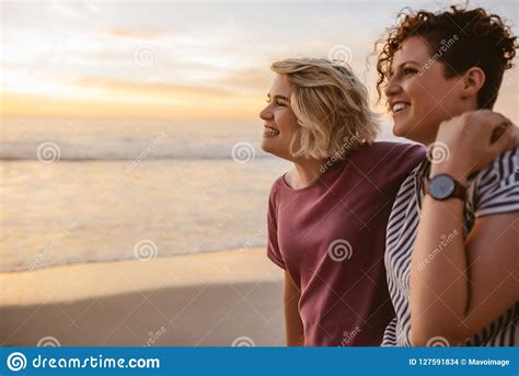 Smiling Lesbian Couple Watching The Sunset Together At A Beach Stock