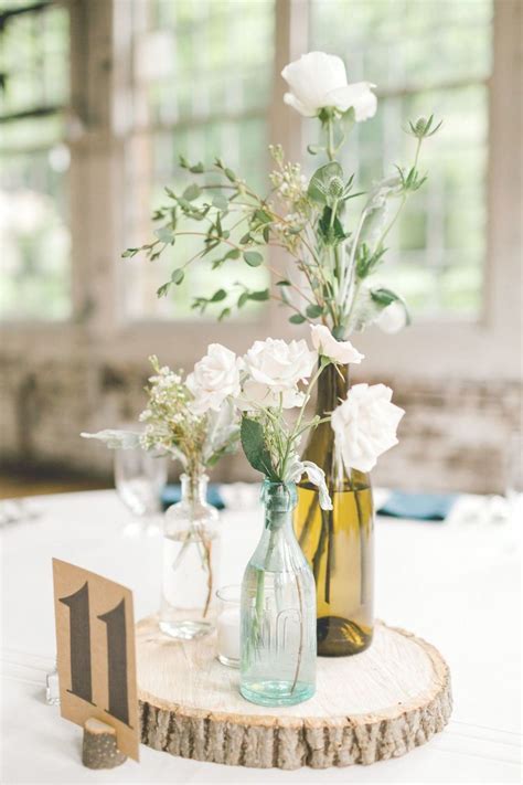 Small Floral Arrangements In Used Wine Bottles On Tables
