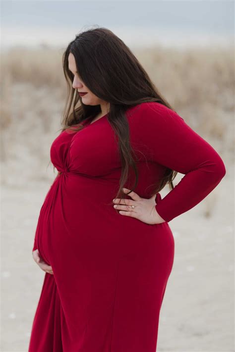 Plus Size Pregnant Woman In Red Dress Looking Down And Holding Her