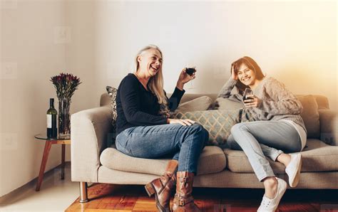Smiling Mother And Daughter Relaxing On A Couch And Drinking Win